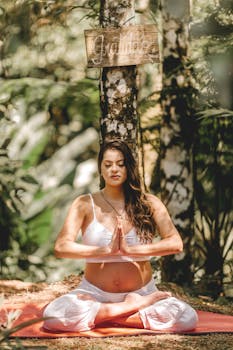 Pregnant woman in meditation pose on yoga mat in a peaceful forest setting.