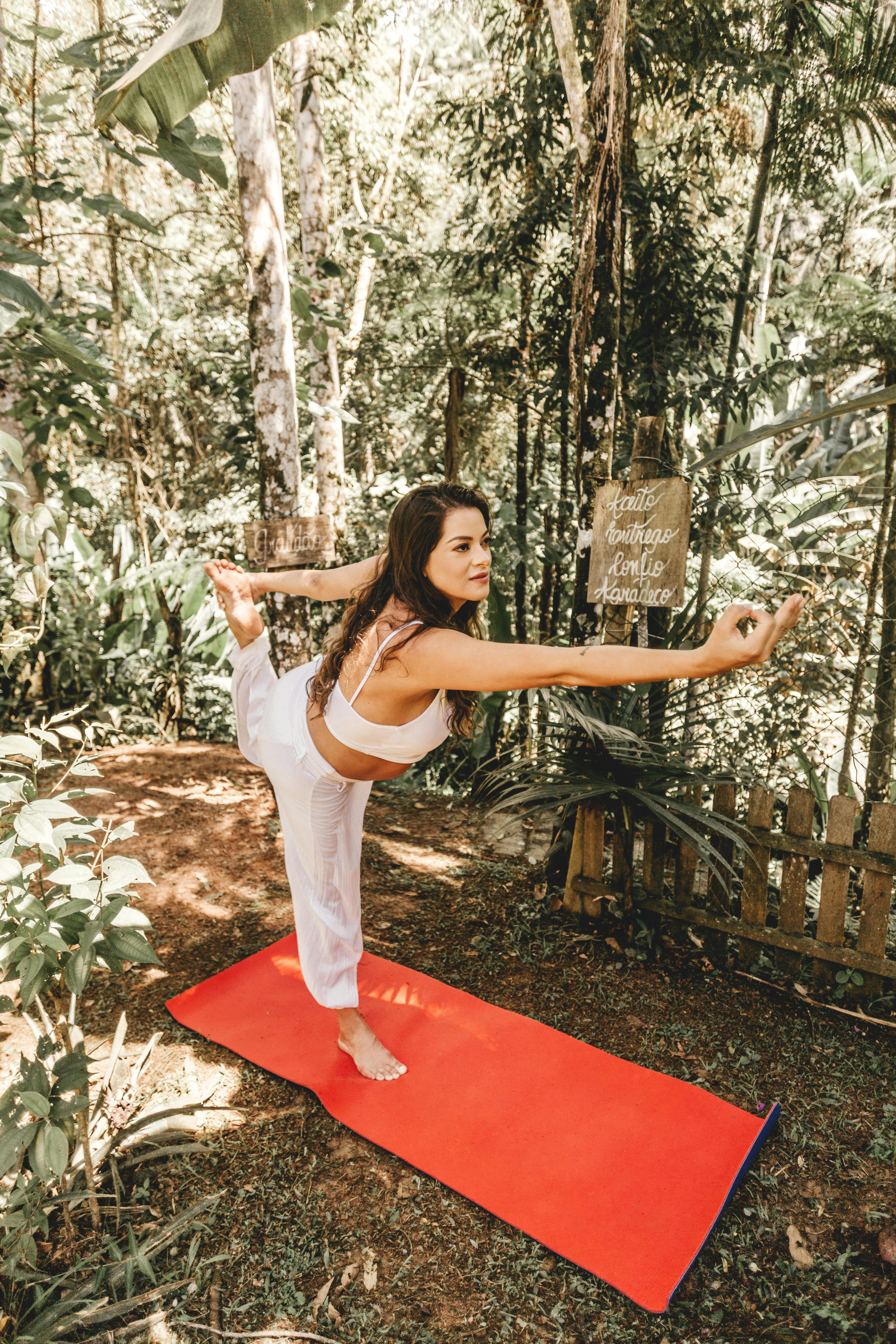 A woman doing a yoga pose on a red mat in a sunlit forest, embodying wellness and serenity.