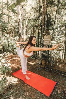 A woman doing a yoga pose on a red mat in a sunlit forest, embodying wellness and serenity.