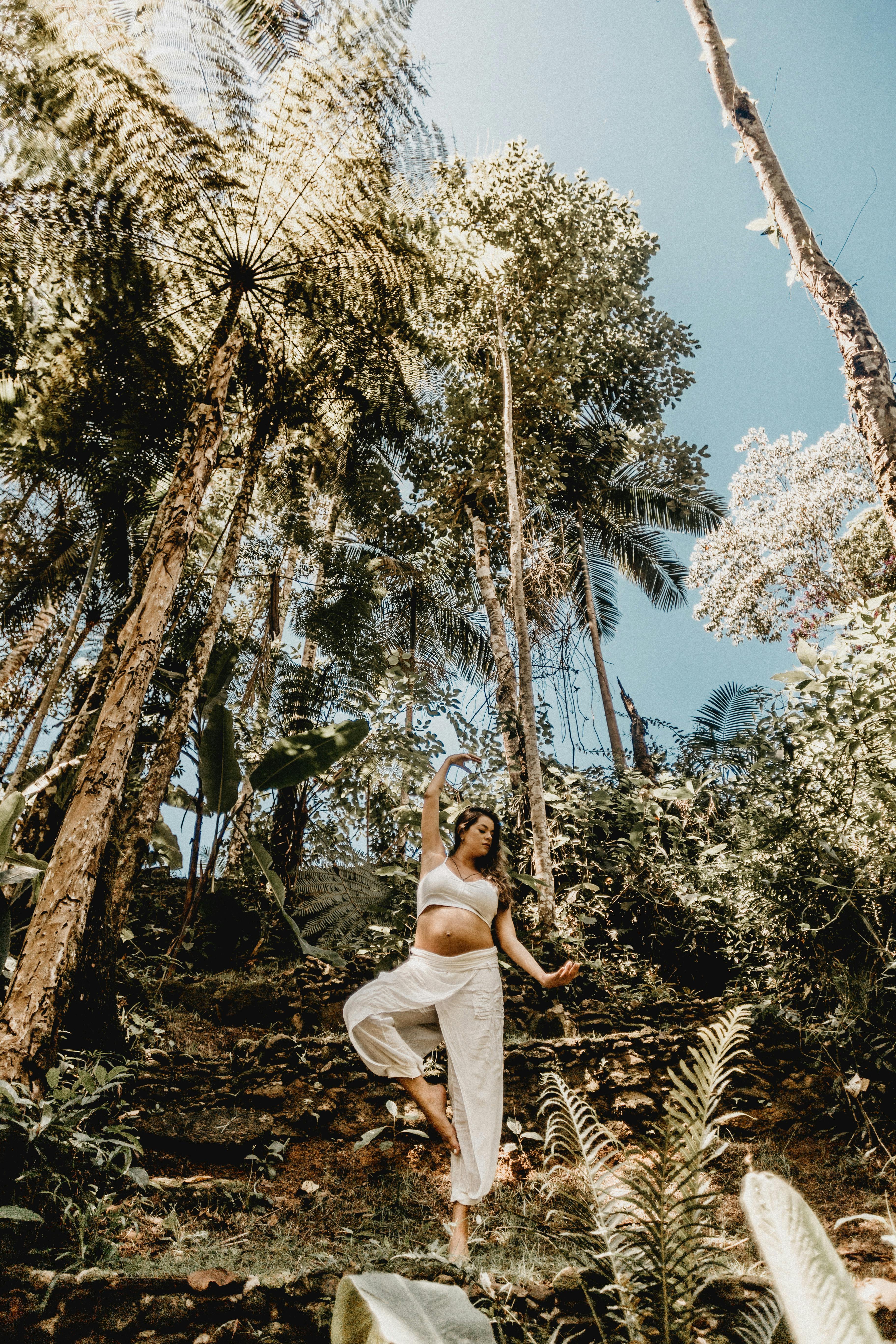 woman standing between palm trees on one leg with an arm raised