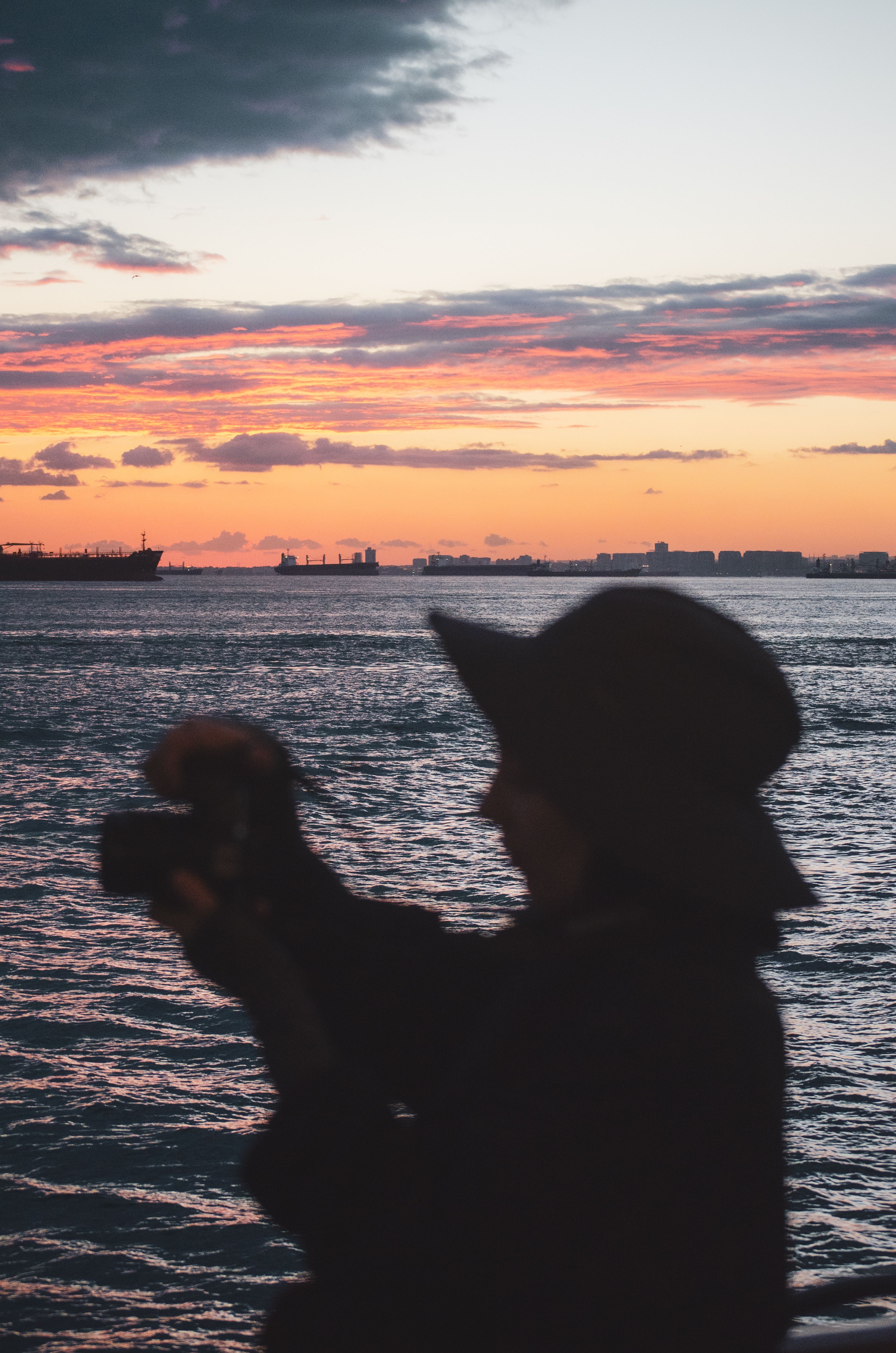 A silhouette of a person taking a photo of a colorful sunset over the ocean.