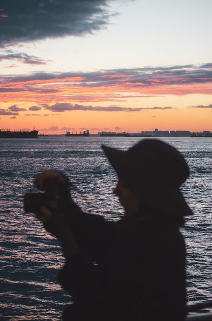A silhouette of a person taking a photo of a colorful sunset over the ocean.