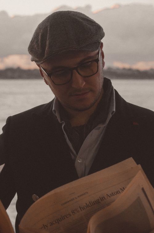 Free A man in a beret cap reads a newspaper near scenic water view. Stock Photo