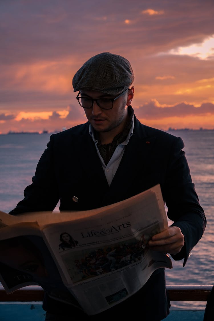 Man Reading Newspaper On Sea At Sunset