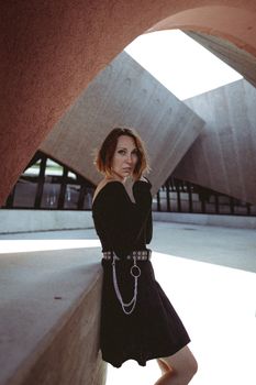 Stylish woman in a black dress posing against abstract architectural background.