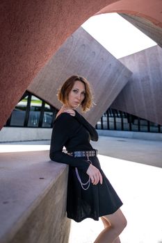 Caucasian woman in a stylish black dress posing against modern architecture.