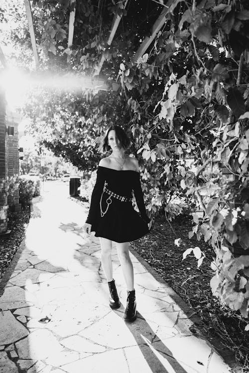 A Grayscale Photo of a Woman in Black Dress Standing on the Street