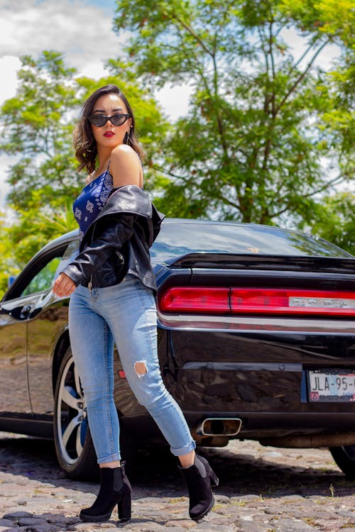 Young Woman in a Leather Jacket and Jeans Posing in front of a Car 