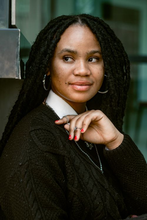 Free A woman with dreadlocks smiles thoughtfully, wearing a black sweater. Stock Photo
