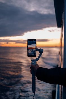 A smartphone on a gimbal capturing a scenic ocean sunset from a boat.
