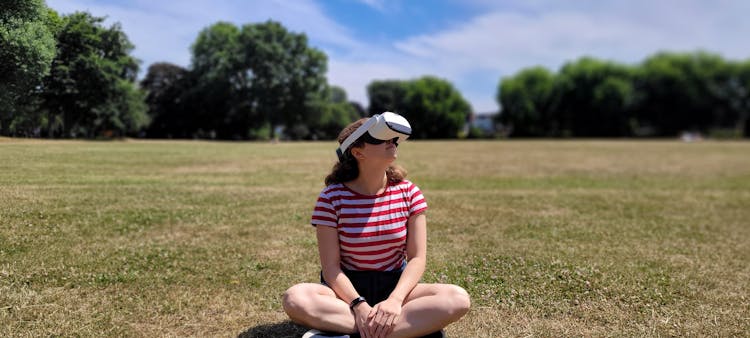  Woman Sitting On Grass Field Wearing VR Goggles