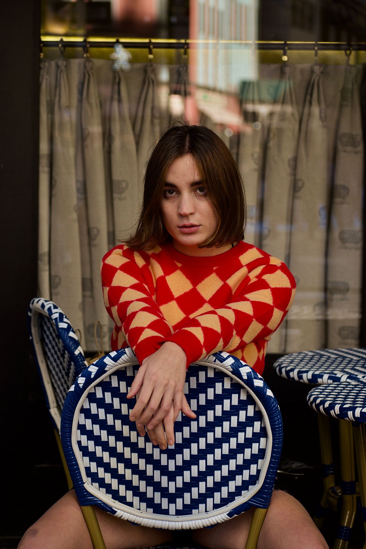Woman wearing a red and peach diamond check knit sweater at an outdoor café