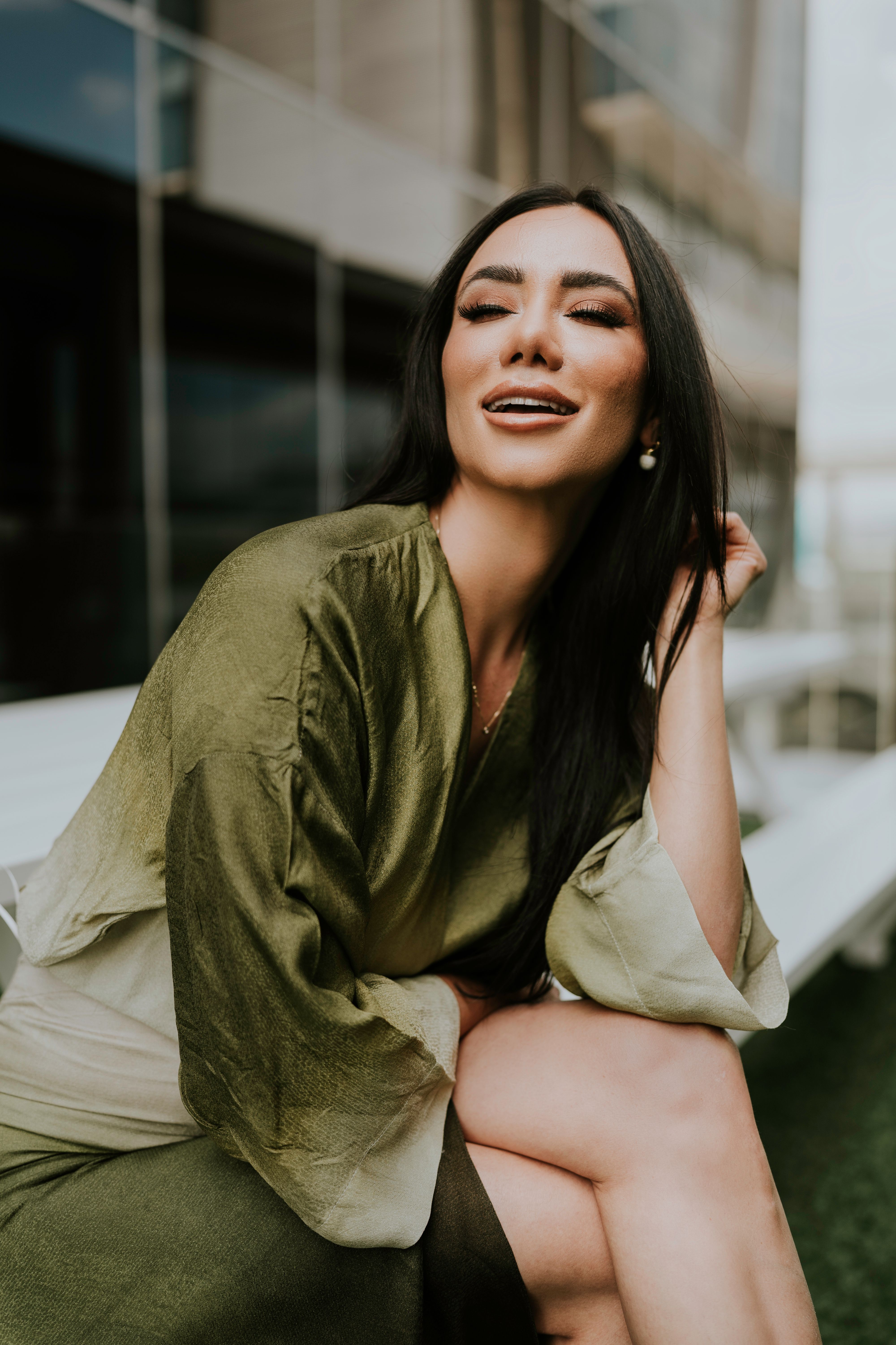 Young woman sitting and smiling in an urban outdoor environment wearing a green dress.
