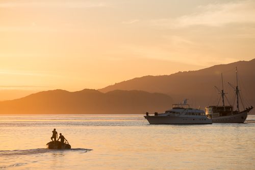 Free Sunset view of boats and mountains with a tranquil ocean setting, creating silhouettes. Stock Photo