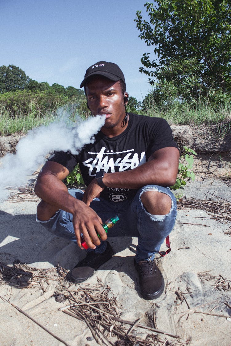 Man Sitting On Ground Smoking Vape