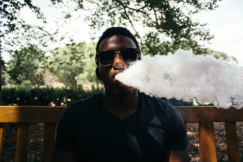 Man in Black Shirt Blowing Out Smoke Under Shade of Tree