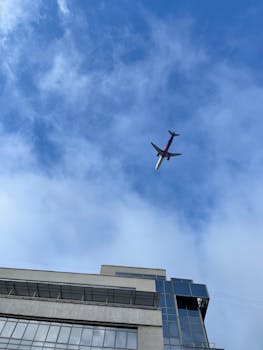 A commercial airplane soars over a modern building in Kiev against a clear blue sky.