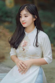 一位身着传统连衣裙的年轻女子在户外优雅摆姿，展现出宁静的时尚风格