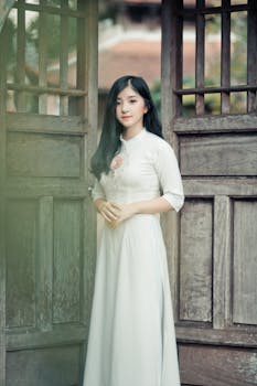 一位身着传统白色连衣裙的亚洲女子站在木门口，显得十分优雅