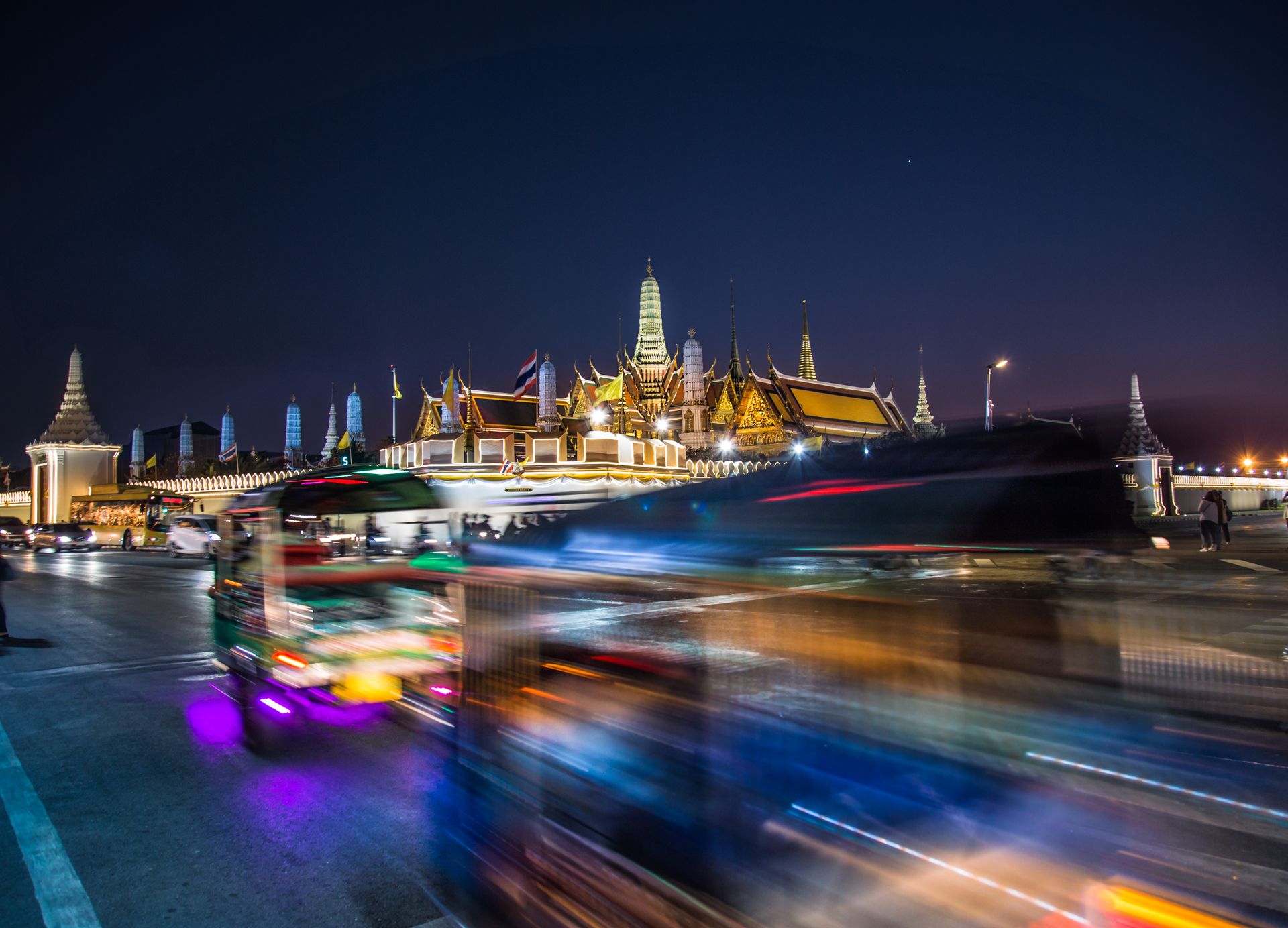 Dynamic cityscape with Wat Phra Kaew illuminated at night in Bangkok, Thailand.