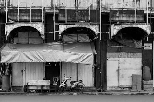 Black and White Photo of Scooter Parked under Abandoned Building