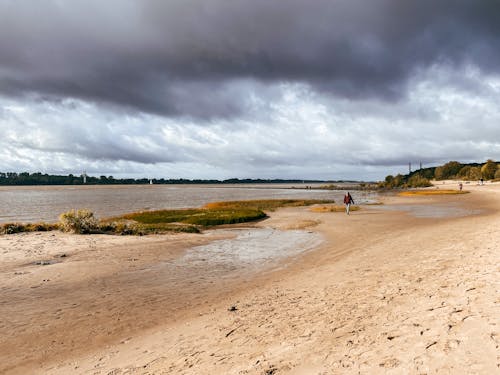 View of People Walking on a Beach beside a Body of Water under a Cloudy Sky 