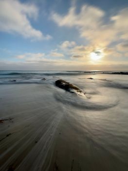 Tranquil ocean scene with rocks and golden sunset over calm waters.