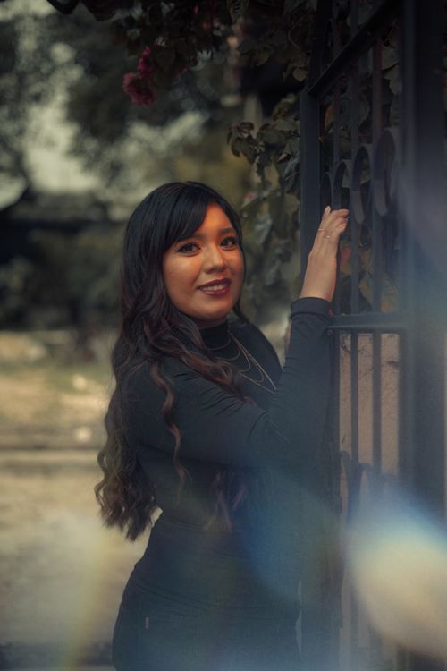 Free Warm-toned portrait of a smiling woman standing by an iron gate outdoors. Stock Photo