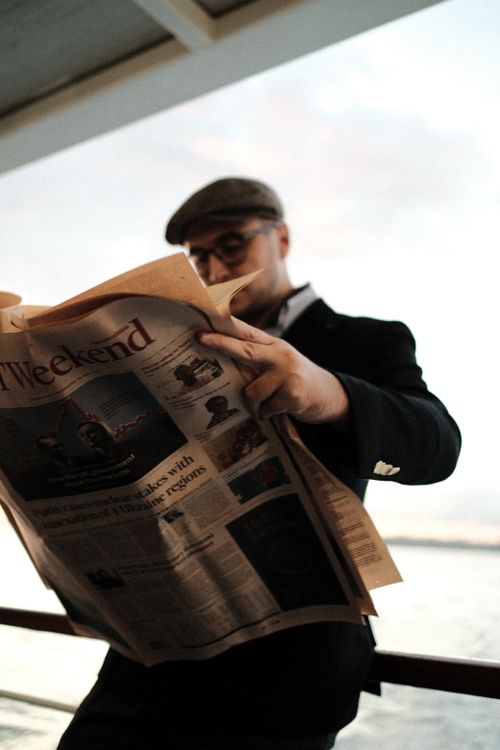 Free Adult man reading a newspaper in a relaxed setting by the waterfront during the day. Stock Photo
