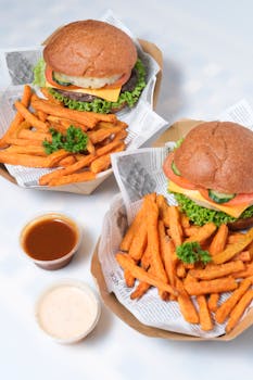 A delightful meal of burgers with vegetables and golden sweet potato fries served with dipping sauces.