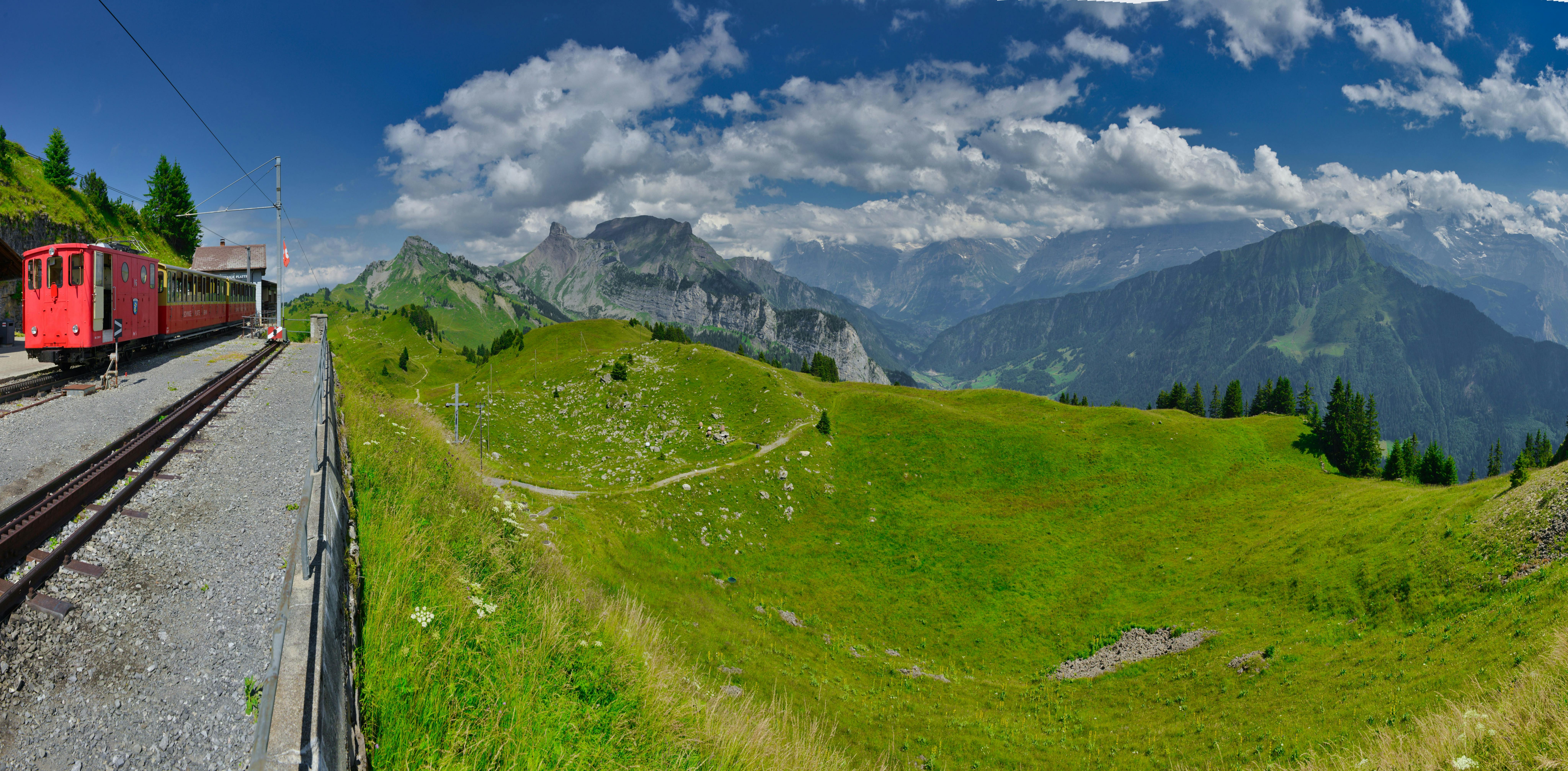 Panoramic view of Schynige Platte with a classic red train and majestic Swiss Alps backdrop.