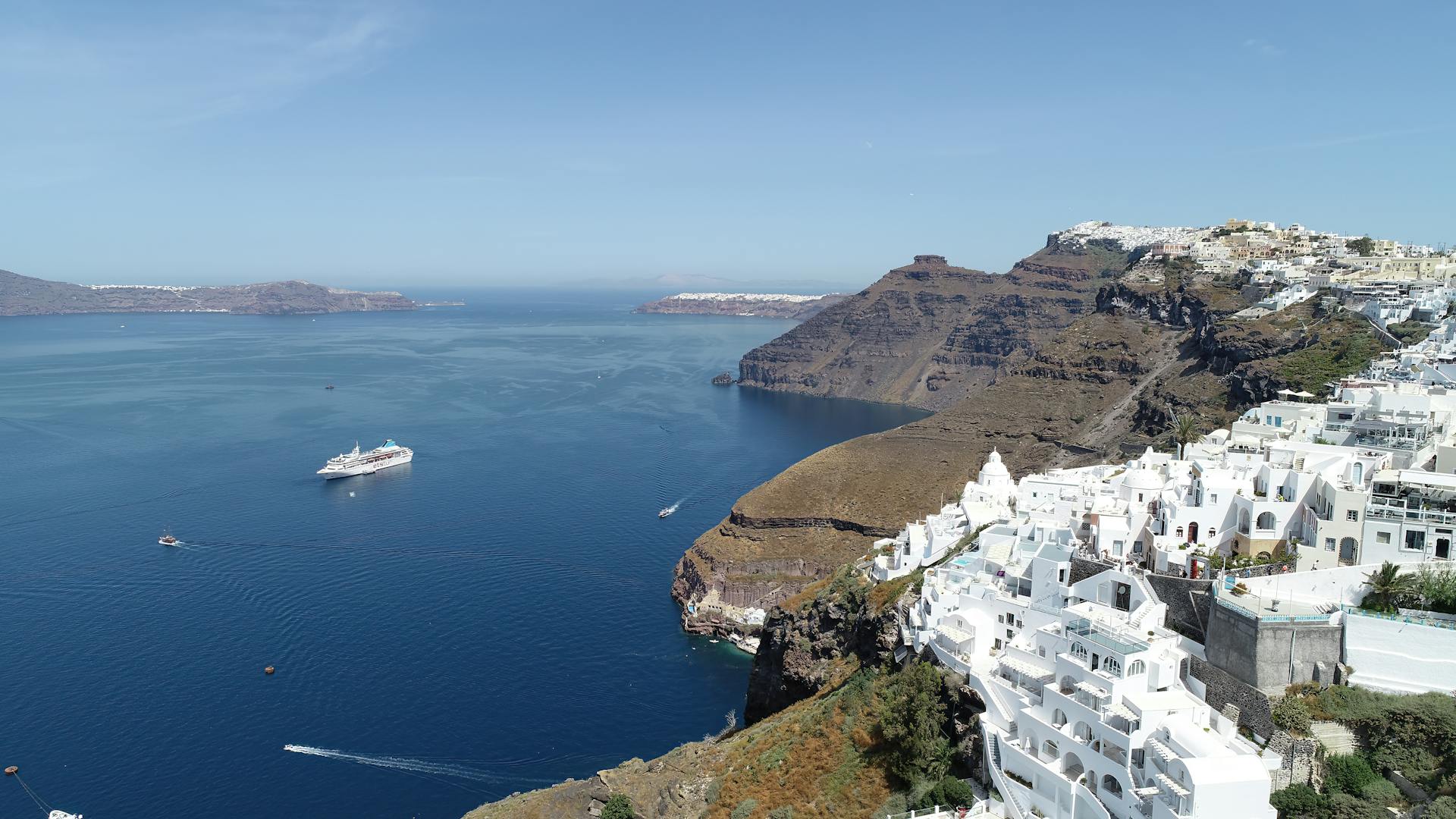 A stunning coastal view of Santorini with white buildings and a cruise ship in the blue sea.