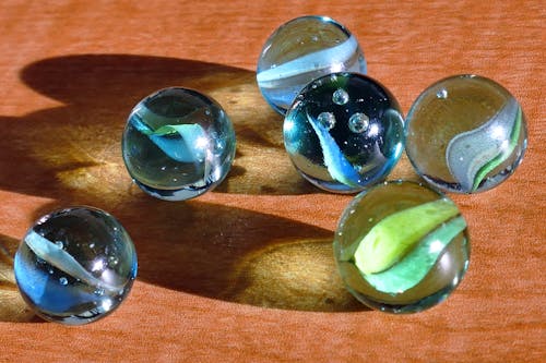 Six Blue and Green Marbles on Brown Surface