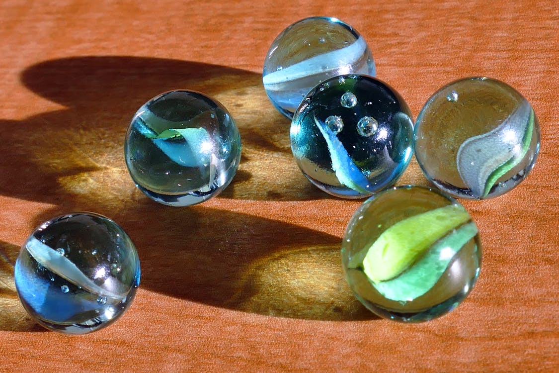 Free Six Blue and Green Marbles on Brown Surface Stock Photo