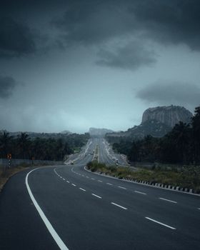 A winding highway leads towards a rocky mountain, under a moody, cloudy sky, capturing the essence of adventure and travel.