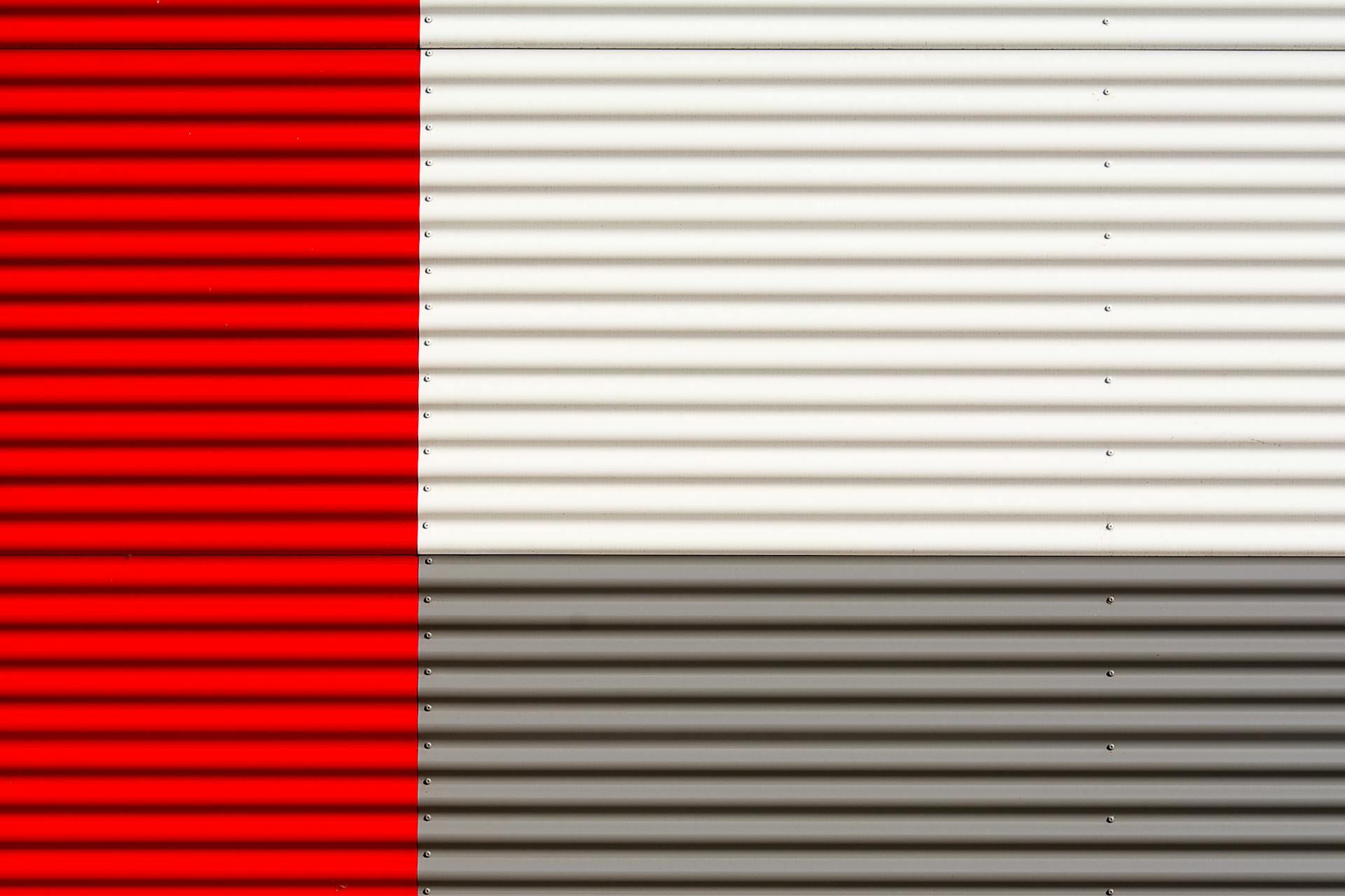 Close-up of a red, white, and gray corrugated metal wall with horizontal stripes.