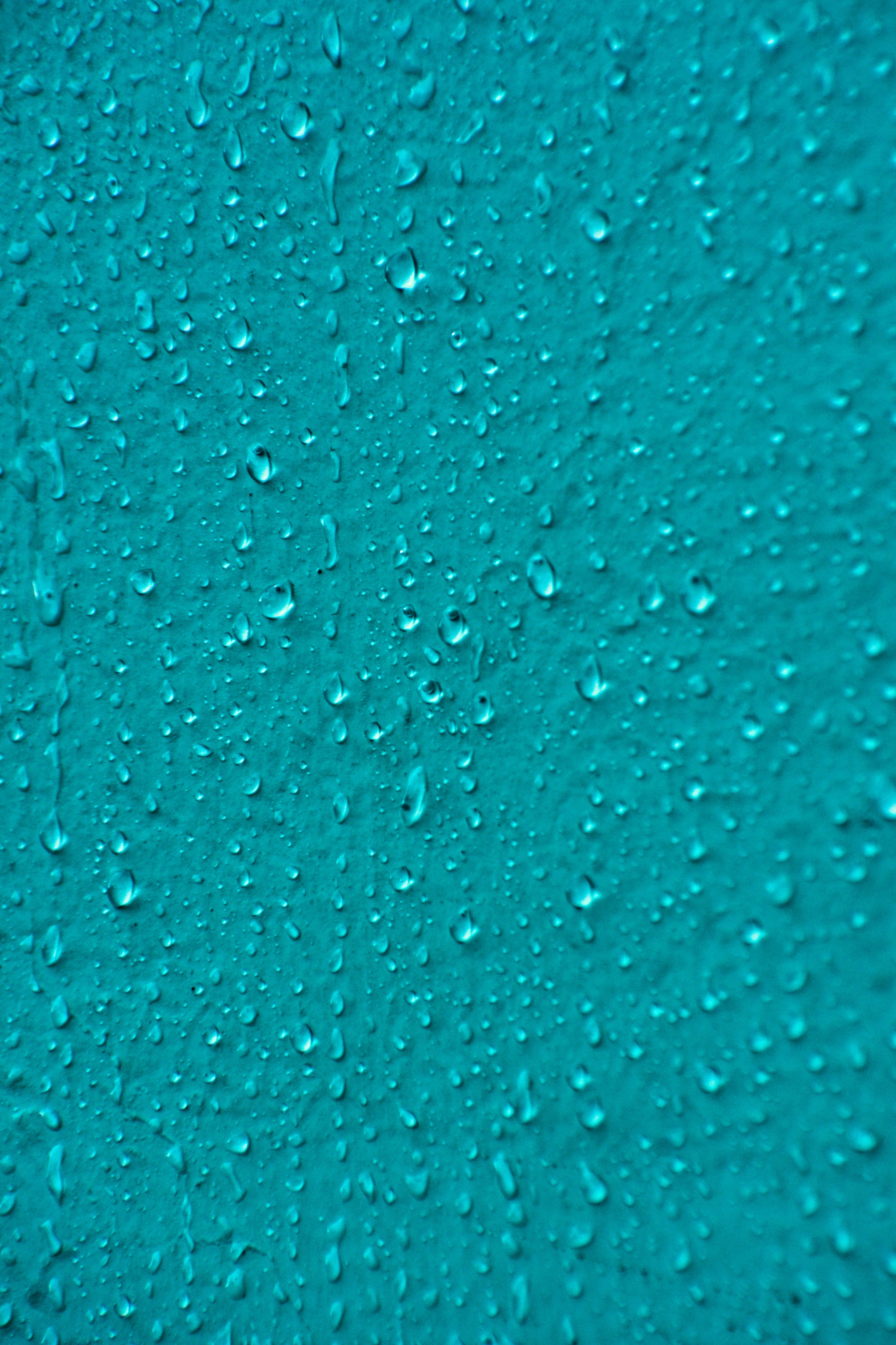 Close-up view of raindrops on a teal surface creating an abstract pattern, ideal for backgrounds.