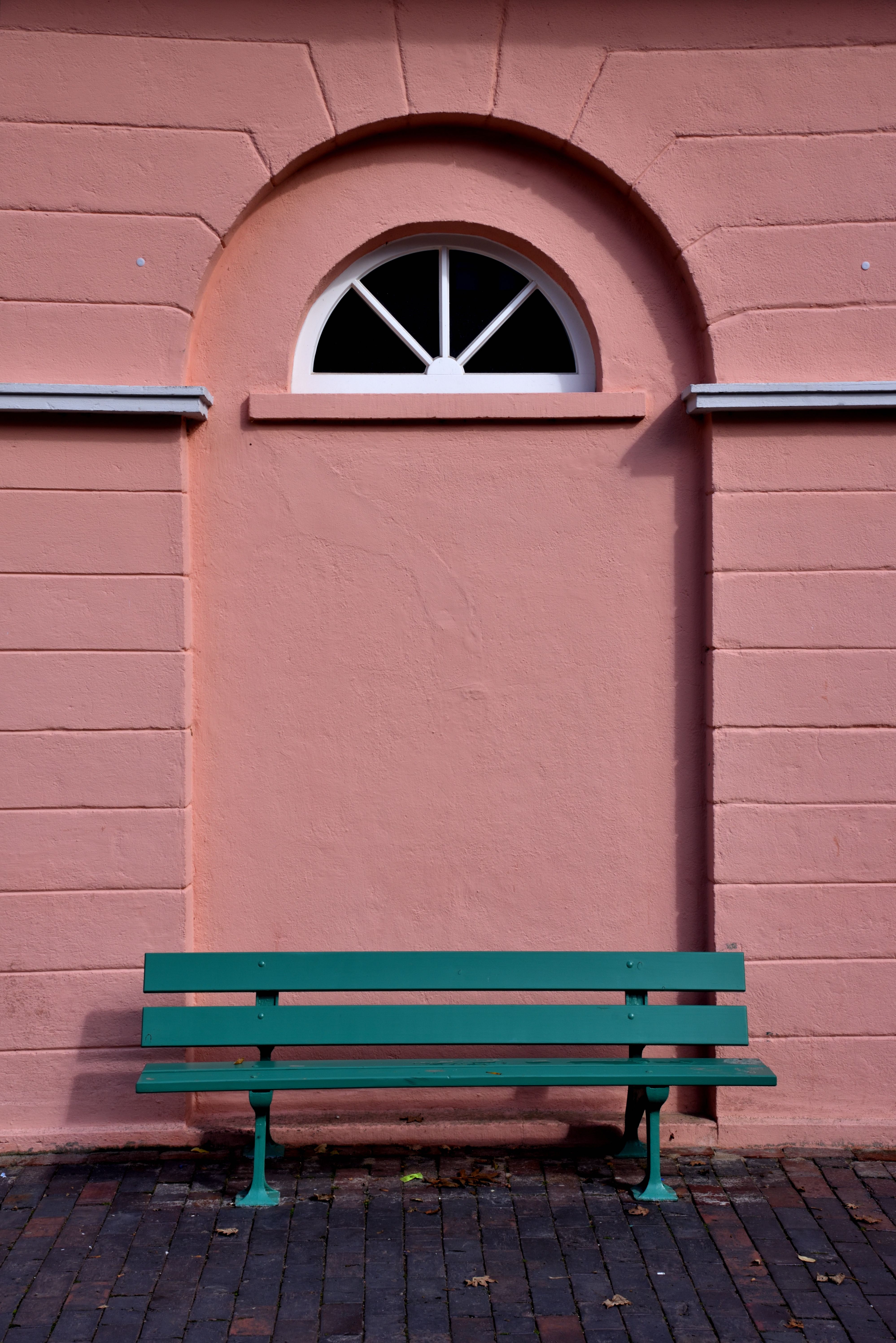 A vibrant green bench sits against a charming arched window and pink wall in Jever, Germany.