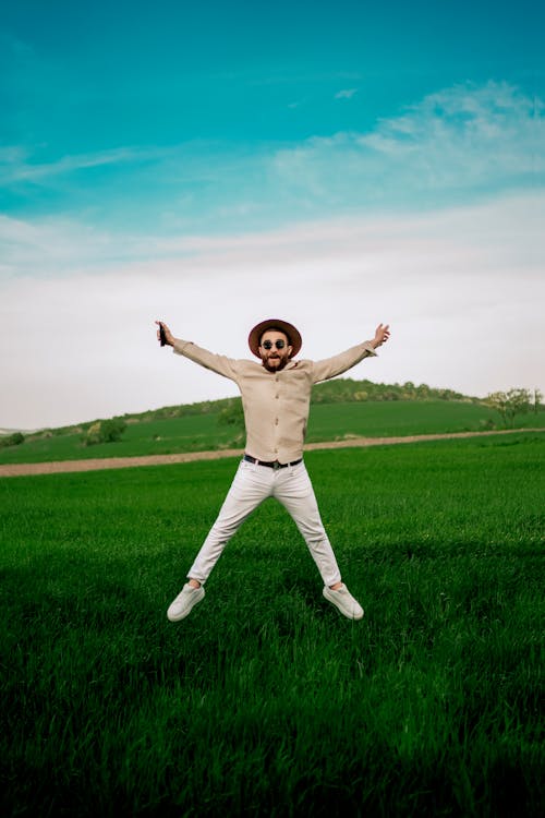 Man Wearing a Hat and White Trousers Jumping in a Green Field