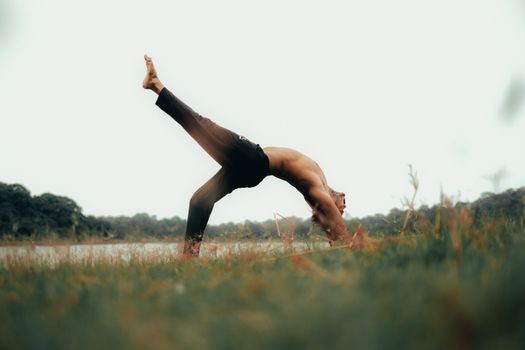 A man performing yoga in a field, showing balance and flexibility in nature.