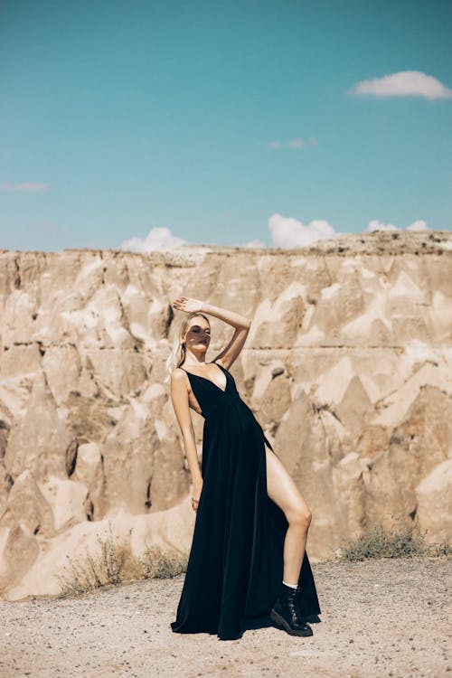 A Woman in Black Dress Standing Beside Brown Mountain
