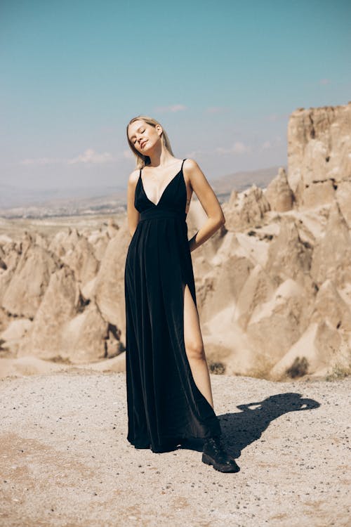 Woman in Black Spaghetti Strap Long Dress Standing Near Big Rocks