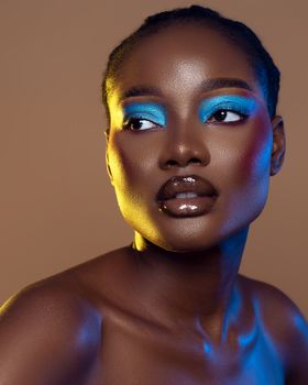 Studio portrait of a woman with vibrant makeup featuring bold blue eyeshadow and glossy lips.