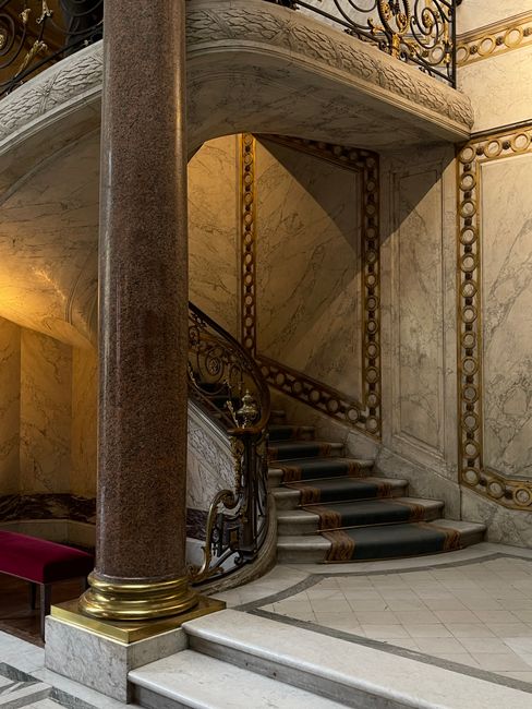 Elegant spiral staircase with ornate railing and marble in a historic Paris building.