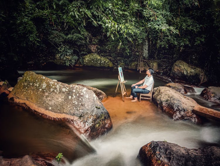 Man Sitting Among Flowing Water And Painting On Canvas 