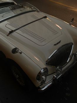 Classic white convertible car with vintage design seen at sunset from a high angle.