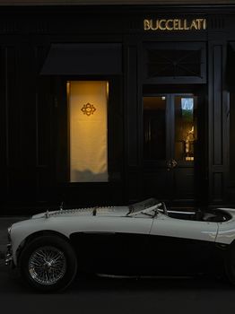 A classic vintage convertible parked outside a luxury store at night.