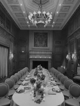 Luxurious dining room with a long table in monochrome, featuring ornate decor and chandelier.