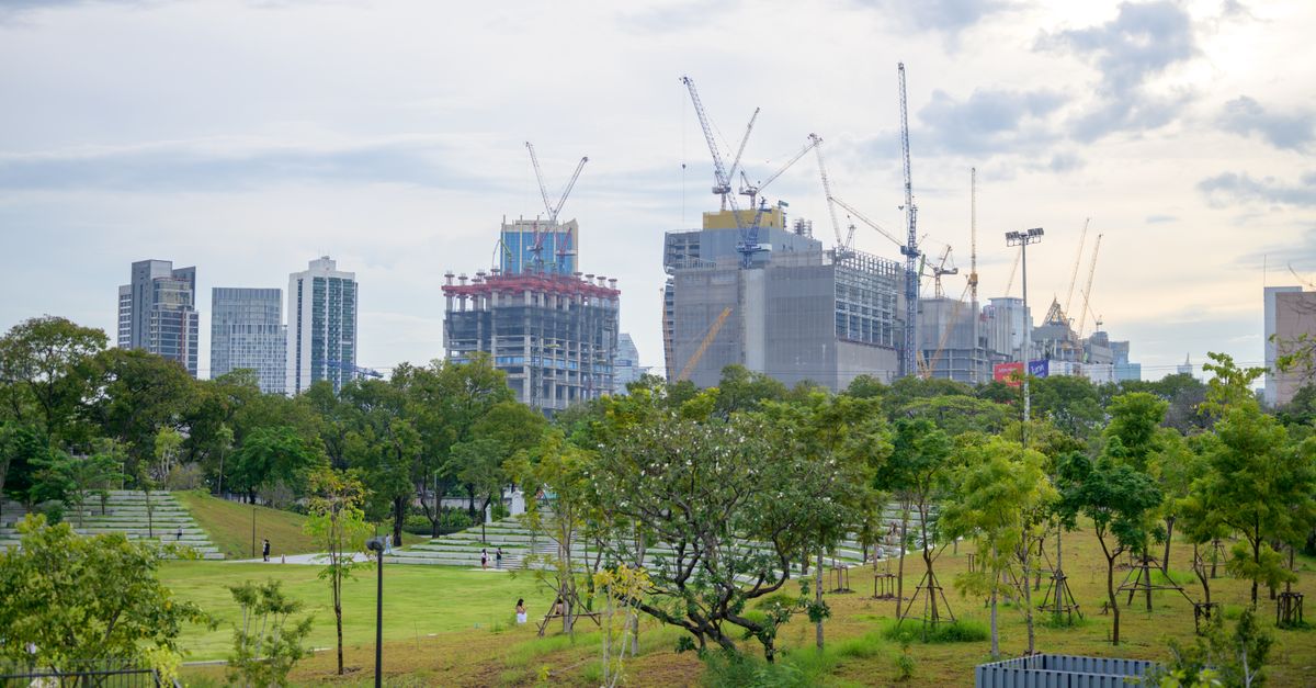 Urban skyline with cranes and skyscrapers under construction amidst green park.