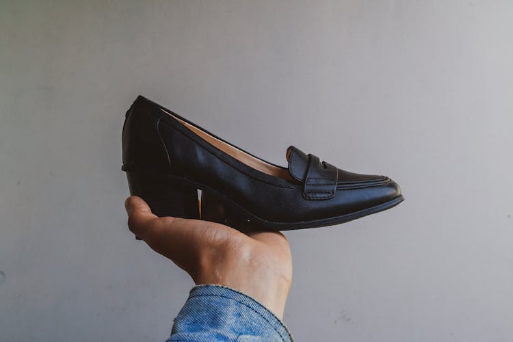 A Person's Hand Holding A Black Leather Shoe